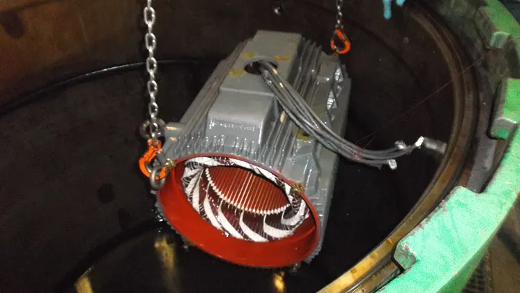 Electric motor being dipped into a varnish tank.